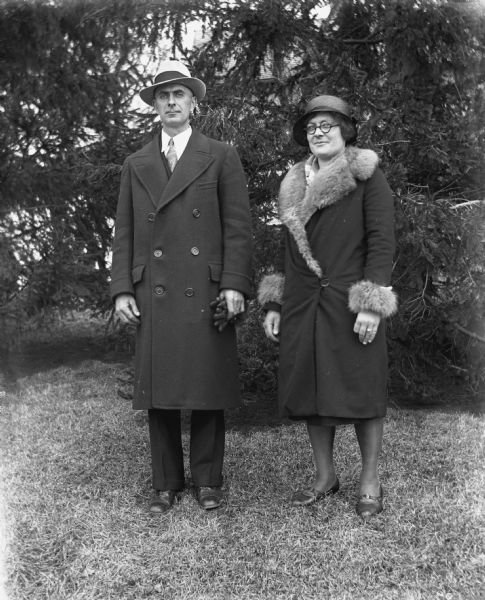 Outdoor portrait of Edgar and Elna Krueger standing in front of several pine trees.
