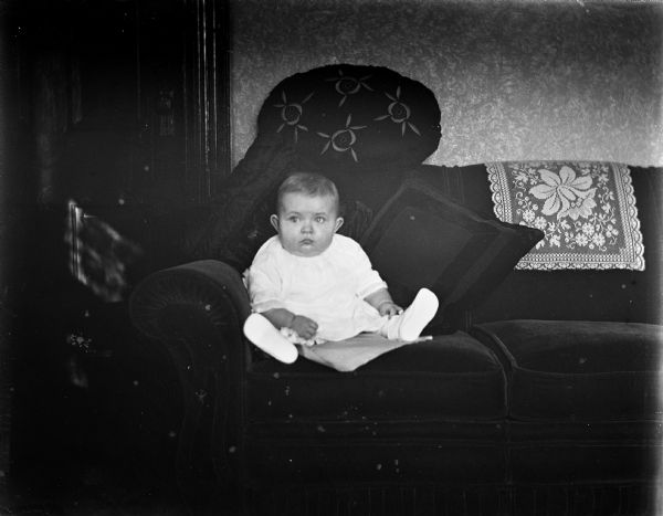 Baby Shirley Krueger propped up on a couch with pillows.