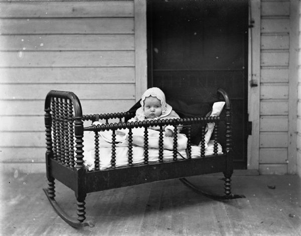 Shirley Krueger propped up with pillows in an old cradle placed on the porch.