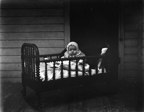 Shirley Krueger, propped up with pillows in her grandfathers old baby cradle which has been placed on the front porch.