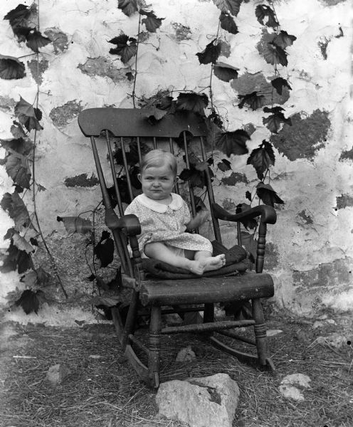 Outdoor portrait of Shirley Krueger sitting in a rocking chair. The chair and the building behind has ivy growing on it.