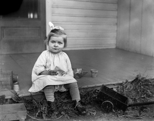 Shirley Krueger sitting on the edge of the porch with several toys around her.