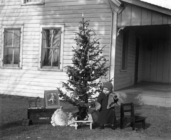 Shirley Krueger standing next to an outdoor decorated Christmas tree. Several of her presents are placed at the base of the tree.