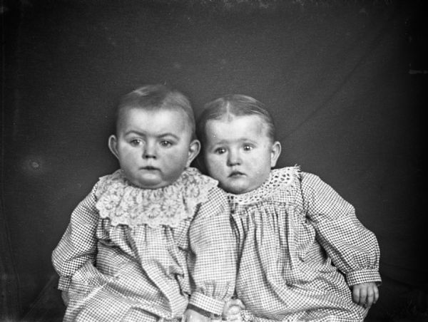 Indoor portrait of Edgar and Jennie Krueger from the waist up, propped against a dark cloth background. The twins are 10 months and 3 days old.