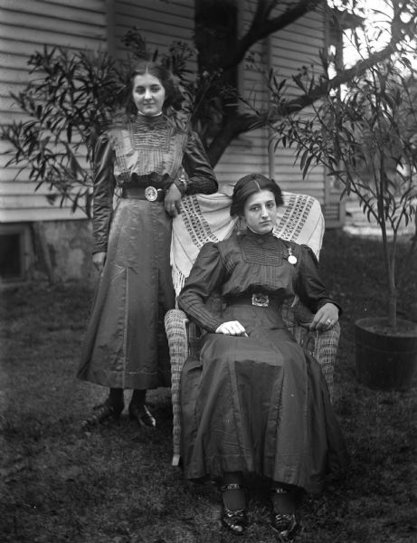 Outdoor portrait of Josie and Esther Bigalk in the yard. Two potted are trees behind them.