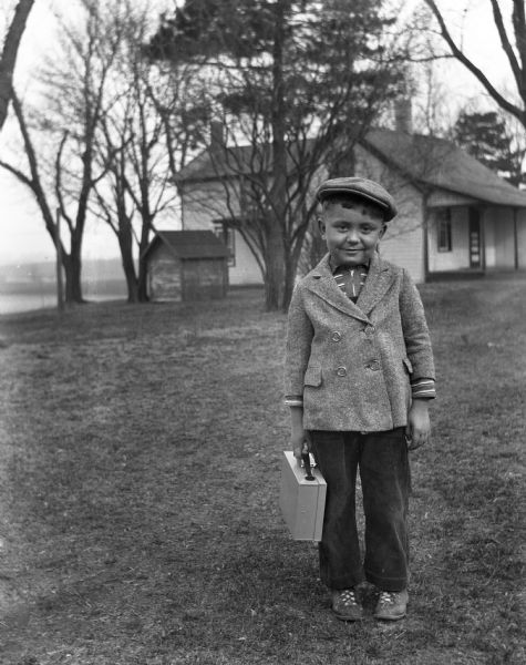 Robert Kruger standing out in the front lawn waiting for the school bus. He is holding a small briefcase that he uses for school.