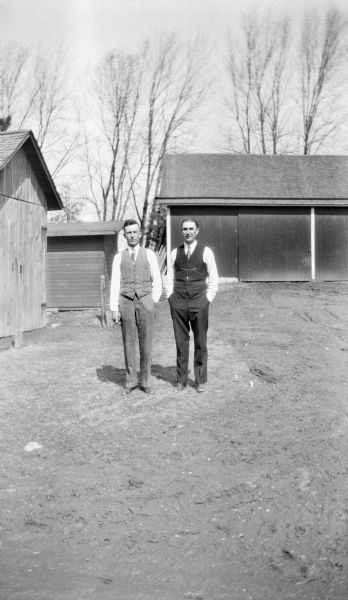 Edgar Krueger and a friend standing amongst farm buildings on the Krueger farm.