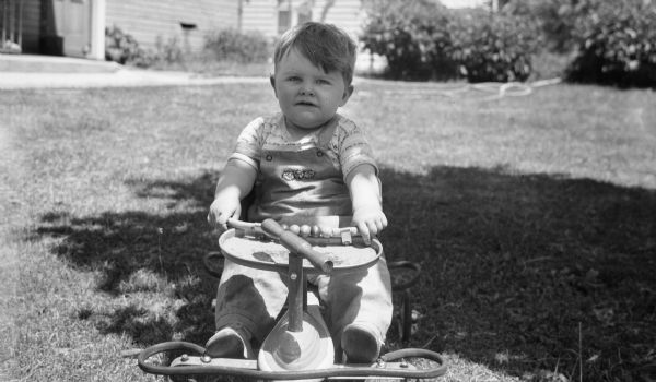 Outdoor portrait of a young boy sitting in a four wheeled bike (walker) on the front lawn.