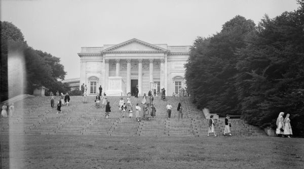 View from lawn of the Tomb of Unknown Soldier and the Arlington Memorial Amphitheater from the base of the stairs leading to the monument. Groups of men and women are walking on the steps and standing near the tomb.