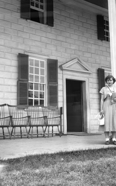 Shirley Krueger standing near one of the columns on the piazza. Several chairs are lined up against the wall to the left of an open doorway.