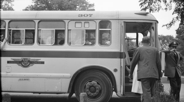 Men and women boarding a coach bus. The bus driver stands outside leaning against the front of the bus. Several people are seated in the bus seats with the windows open. On the side of the bus is printed: "Arnold Lines."