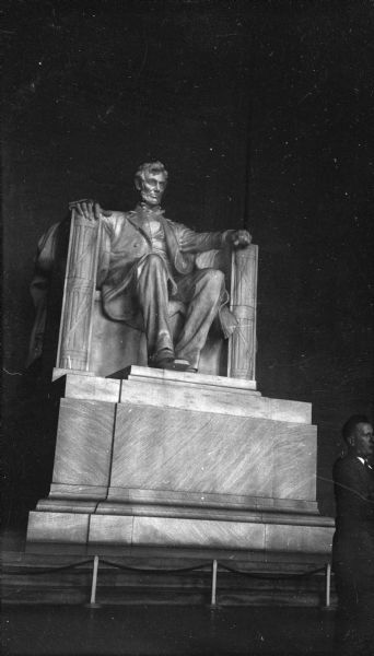 View of the Lincoln Statue inside the Lincoln Memorial. A man stands in front of the statue on the right.