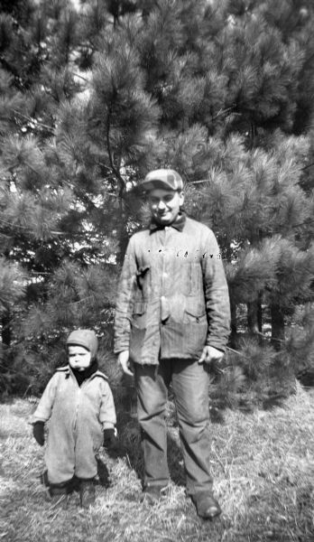 Robert Krueger standing with his nephew, Glenn Oestreich, in front of a row of pine trees.