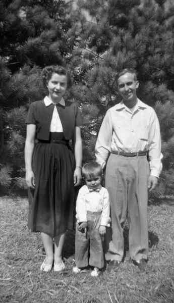 Outdoor portrait of the Adelbert Oestreich family posing in front of a row of trees. From left to right: Shirley Krueger Oestreich, Glenn Oestreich, and Adelbert Oestreich.