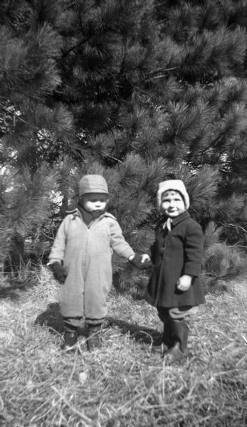 Glenn Oestreich holding hands with a young girl in front of a row of pine trees.