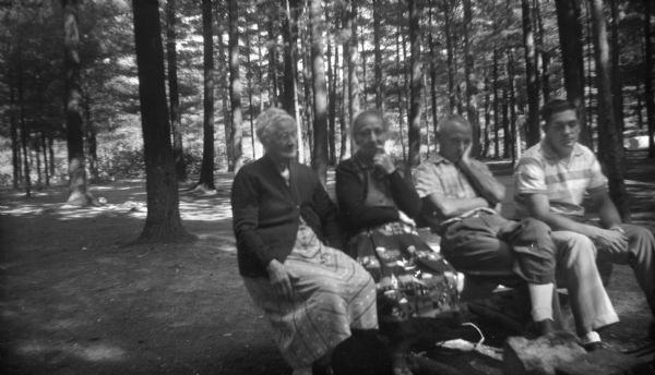 Group portrait of Robert Krueger sitting with two elderly women and another man on a bench in the woods.