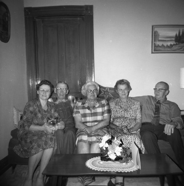 Elna Krueger is squeezed between two other couples on a couch. A cat sits in the lap of the woman on the far left.