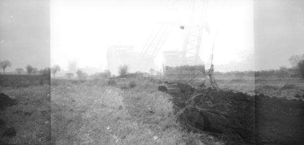 Double exposure of a drag bucket digging dirt in a field.