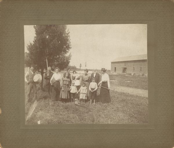 Asa Curtis Bennett family holding cranberry rakes and other manual farm implements. The family is gathered around an owl standing on the ground in front of them.