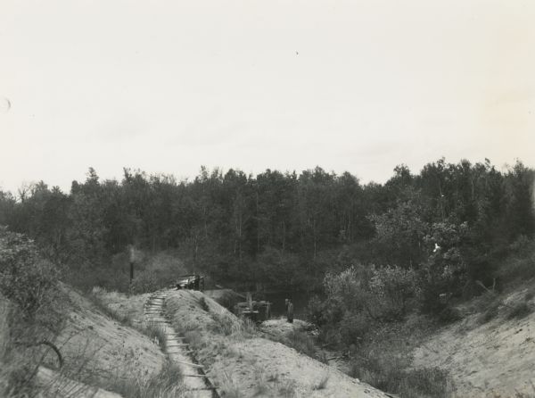 Construction of a new drainage and water supply line for a cranberry marsh. Two men are standing on the right near the water.