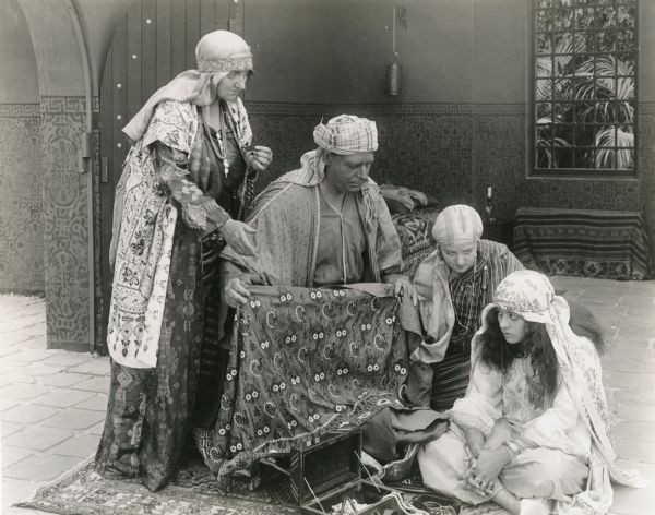 Sitting cross-legged on the floor, the Algerian girl Hafsa (played by Lenore Ulric) is offered jewelry and fine fabrics. Also in the scene, there appear to be Lucille Ward (Lella Sadiya), Joe Massey (the old sheik), and Estelle Allen (Zorah).
