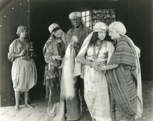 The Algerian girl Hafsa (played by Lenore Ulric) has joined hands with Zorah (Estelle Allen). Behind them are a servant and, apparently Lucille Ward (as Lella Sadiya) and Joe Massey (as the old sheik). The caption typed on the back of the print reads: "The Sheik's ominous marriage gifts."