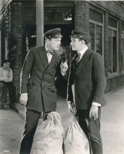 Two seamen, Matt Peasley (played by Thomas Meighan) and Murphy (Hugh Cameron), stand in a San Francisco street with their seabags at their feet in a publicity still from "Cappy Ricks" (Lasky 1921).