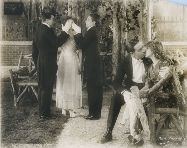 Edith Henderson (played by Boots Wall) has her eyes covered by two young men as Jack Henderson (Owen Moore) kisses Mercy Baxter (Mary Pickford) on a bench in the rose garden. The original caption printed on the photograph is "The Co-Operative Kiss," while the back of the photograph carries the caption in pencil, "And Mercy's husband fell in love with his wife again."

The young man between Boots Wall and Owen Moore appears to be Ernest Truex in his first film role, playing Wally Henderson.