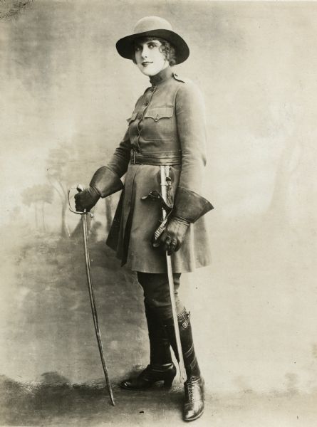 Pearl White stands in front of a painted studio background, sword in hand, wearing the female version of a U.S. Army cavalry uniform.