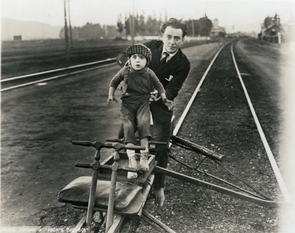 Henry Peck, the "bad boy" of the title played by Jackie Coogan, and Dr. Martin (played by Wheeler Oakman) are on a railroad velocipede handcar staring at what must surely be an oncoming locomotive (First National 1921).