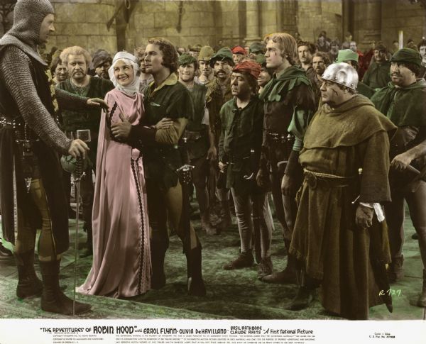 King Richard the Lionhearted gives Maid Marian and Robin Hood permission to marry in one of the last scenes from Michael Curtiz's 1938 "The Adventures of Robin Hood" (First National 1938). From left to right, the first row of actors in this stencil-colored publicity still are: Ian Hunter (playing King Richard), Alan Hale (Little John), Olivia de Havilland (Maid Marian), Errol Flynn (Robin Hood), Herbert Mundin (Much), Patric Knowles (Will Scarlet), and Eugene Pallette (Friar John).
