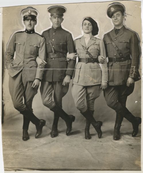 Elsie Janis, in military uniform, stands arm-in-arm with three soldiers in a publicity photograph for the musical revue "Elsie Janis and Her Gang." They wear dress uniforms with jodhpurs and hats.