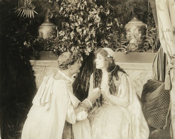 Romeo (played by Harry Hilliard), on his knees, clasps Juliet's (Theda Bara) hand in a romantic scene still in the Fox production "Romeo and Juliet" (Fox 1916).