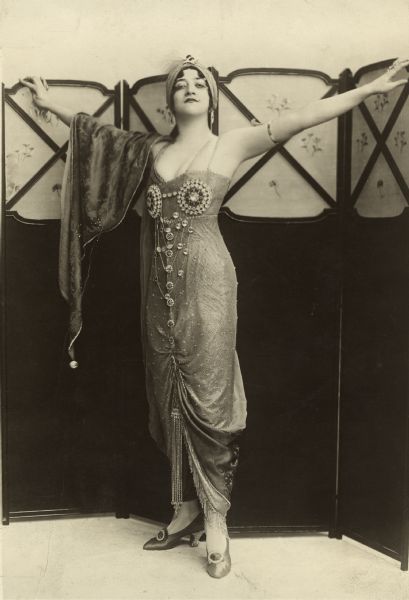 Dorothy Jardon is dressed as Bimboula, a Persian woman, from the musical comedy "Oh! Oh! Delphine" in which she appeared at the Shaftsbury Theatre in London. She wears a remarkable costume jewelry brassiere outside her dress.