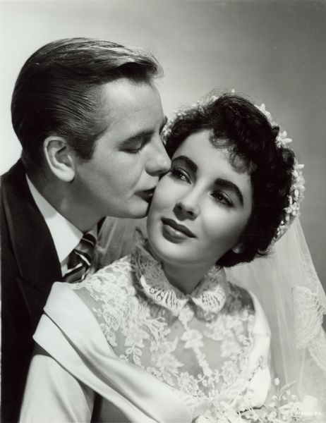 Don Taylor (playing Buckley Dunstan) is kissing Elizabeth Taylor (as Kay Banks) in a publicity still from "The Father of the Bride" (MGM 1950). Elizabeth Taylor wears a white wedding dress and veil.