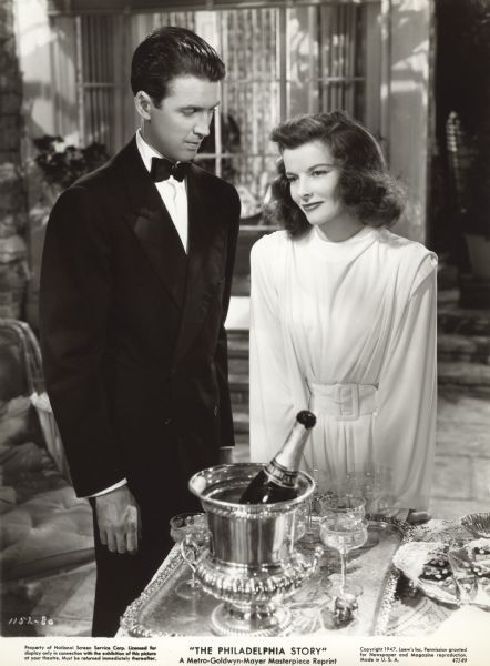 James Stewart and Katharine Hepburn stand by a table with hors d'oeuvres and champagne in a scene still from "The Philadelphia Story" (MGM 1941).