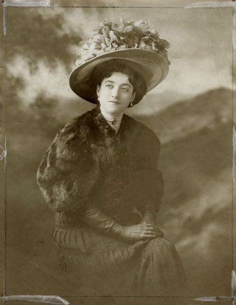 Dorothy Jardon in a White Studio publicity photograph for her first Broadway appearance, the musical comedy "The Merry-Go-Round," which opened at the Circle Theater in April. She sits in front of a painted backdrop, and is wearing street clothes, including a short fur jacket and a large hat heaped high with flowers and feathers.
