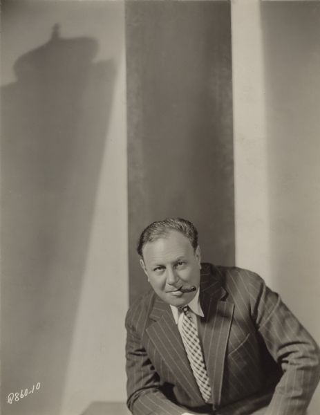 Paramount Pictures studio portrait of Emil Jannings in coat and tie with a cigar in his mouth.
