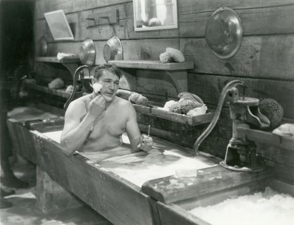 Sergeant Donald MacDuff (played by Victor McLaglen) shaves while bathing in a long wooden trough in "Wee Willie Winkie" (Fox 1937).