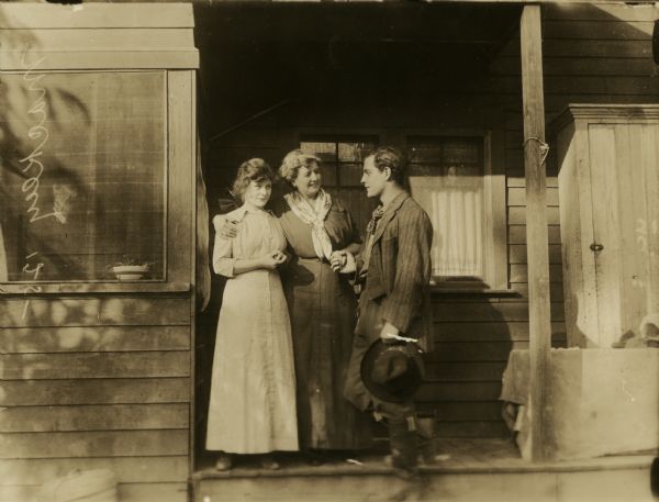 Although identified as a scene still from "Above Par," this photograph of the actors Florence Crawford, W.E. Lawrence, and an unidentified actress playing Crawford's mother is more likely to be a scene set on a farmhouse's back porch from "The Deputy's Chance That Won," another 1915 Reliance production. A note written on the negative reads "Mackley 125-." Arthur Mackley directed and acted in "The Deputy's Chance That Won."