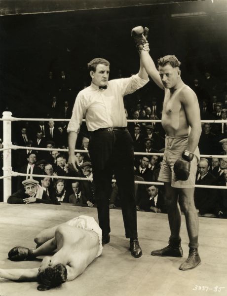 A boxing referee raises the gloved hand of Pat Glendon, Jr. (played by Reginald Denny) to mark him the winner of the bout by knockout in this scene still from "The Abysmal Brute" (Universal 1923).