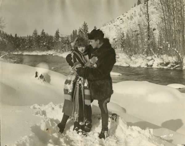 Jen Galbraith (played by Betty Compson) is embraced by Sergeant Flaherty of the Canadian Mounties (Tom Moore) in a snowy wilderness by a rushing river in a scene still for the 1922 Famous Players-Lasky silent film "Over the Border."