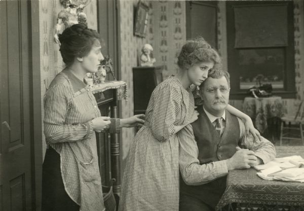Mrs. Carter (played by Mary Alden) and her daughter Helen (Bessie Love) try to comfort John Carter (Wilfred Lucas) their unemployed breadwinner in this scene still from the silent film "Acquitted" (Fine Arts 1916).