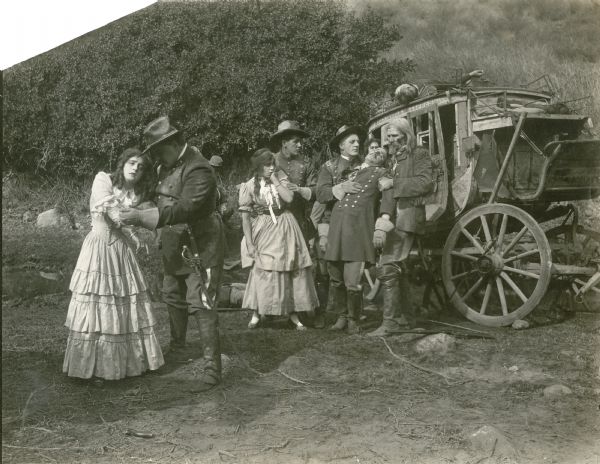 In the left foreground Ethel Grandin is comforted by a U.S. Army cavalry officer. Behind them other officers and a woman standing by a Wells Fargo stagecoach are recuperating from an attack in this scene still from the one-reel silent film "Across the Plains," also known as "War on the Plains." J. Barney Sherry appears to be the actor whose gloved hand on the chest of the swooning officer.