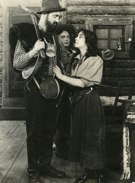 A gold prospector with pick, canteen, and pan gets an emotional greeting or goodbye from Ethel Grandin in this scene still from "Across the Plains," also known as "War on the Plains." A note on the back of the print lists the actors Red Mack and Charlie Westin, but other sources identify the English actor Howard Davies in the role of the prospector.