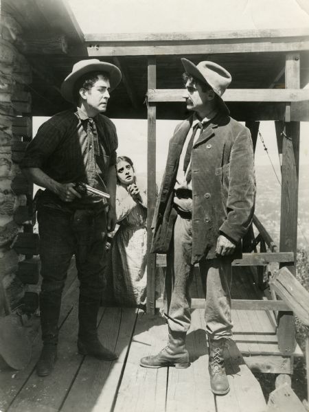 William E. Shay has pulled a pistol on another actor in western dress as Ethel Grandin watches, on her knees with hands clasped in a scene still from "Across the Plains," also known as "War on the Plains."