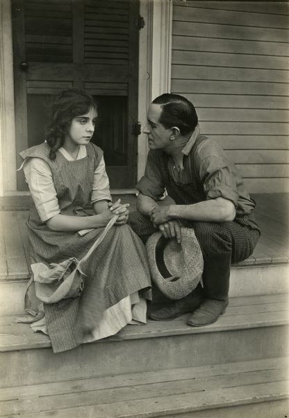 Ethel Grandin and William E. Shay are sitting on porch steps talking in a scene still from "Across the Plains," also known as "War on the Plains."
