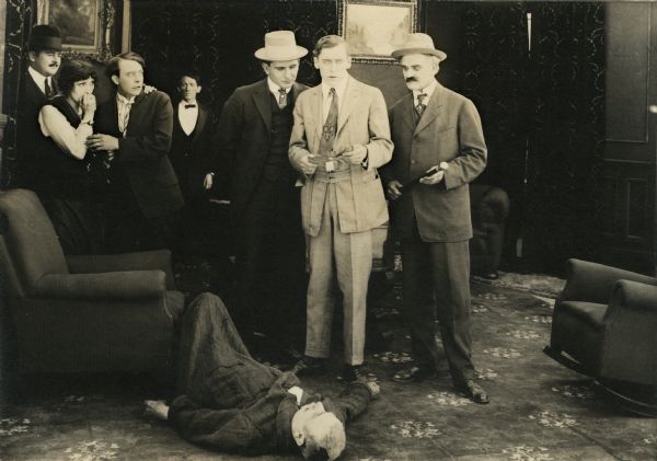 Mr. Pepper (played by Charles Lee) lies dead upon the floor while seven other characters stand about the room in attitudes of shock and bewilderment. On the left is Jane Pepper, the slain man's daughter (played by Irene Hunt). Her arm is around Sim West (Vester Pegg). In the middle holding a paper found clutched in the dead man's hand is her brother (Jack Conway). Looking over his shoulder is the actor William Lowery.