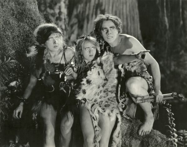Three young cavemen--cavepersons?--react in fear to an offscreen threat. From left to right the actors are Anna Q. Nilsson, Pauline Garon, and Theodore Kosloff. All wear elaborate prehistoric fur costumes and heavy makeup, especially Kosloff who has a putty nose and large false eyebrows and teeth.