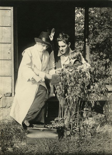 Dr. Jane Bixby (played by Florence Lawrence), wearing a white duster and with her medical bag by her feet, wraps a bandage around a child's ankle on the porch of a modest house. Joe Buford (Owen Moore) holds the child on his lap.
